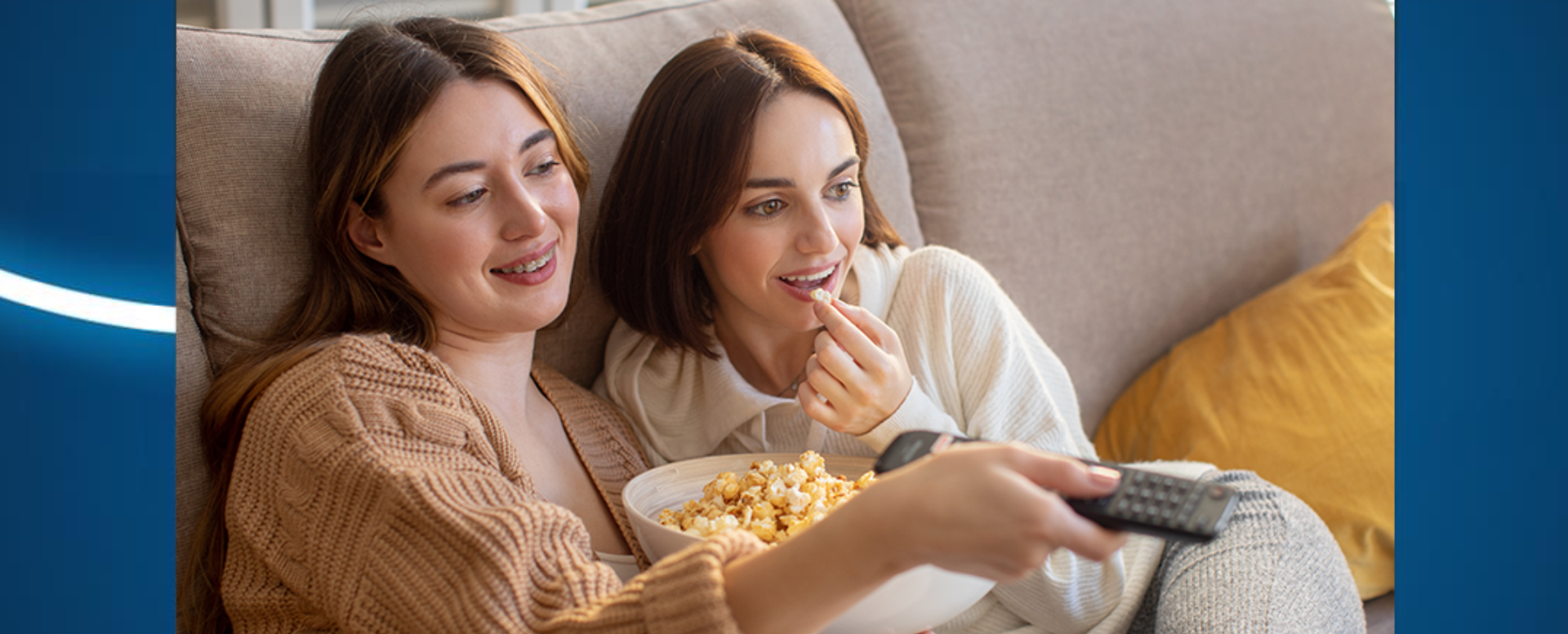dwie dziewczyny siedzą na kanapie, jedna z nich trzyma w ręce pilot i oglądają coś
