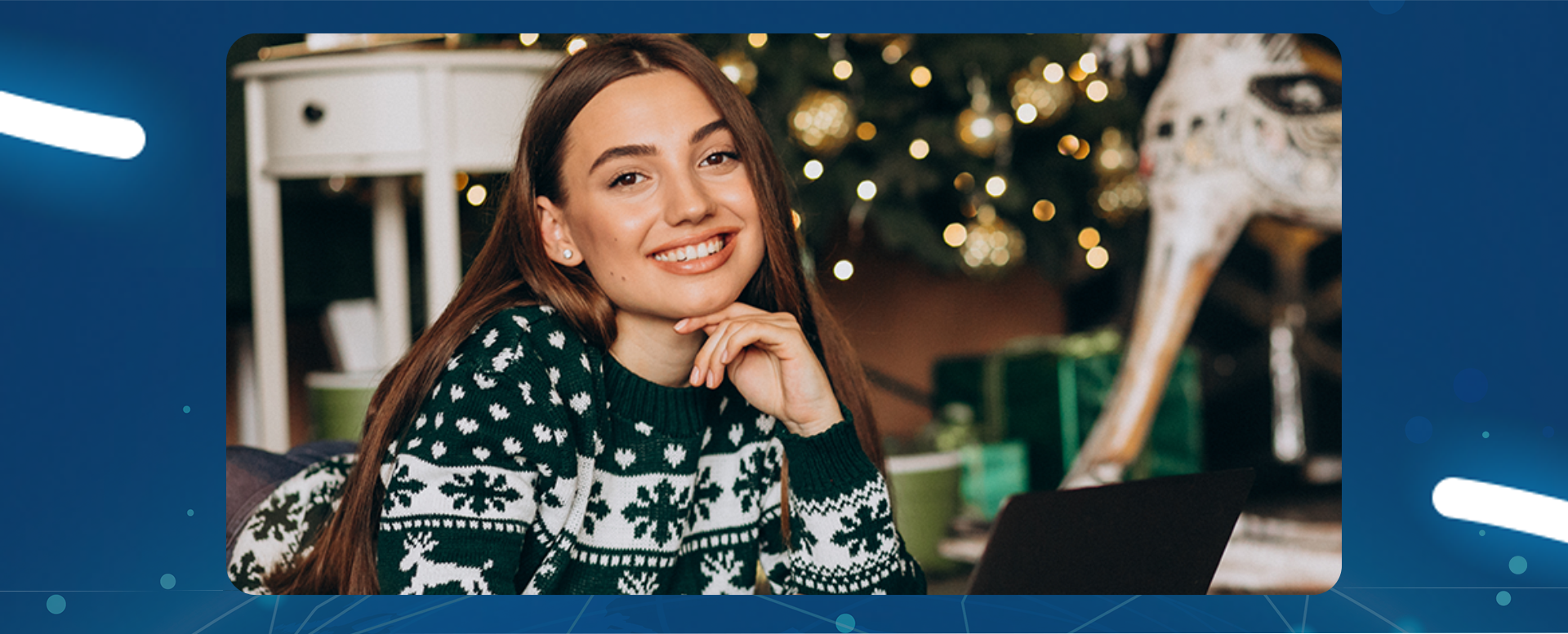 uśmiechnięta dziewczyna siedzi przed laptopem, w tle ozdoby świąteczne