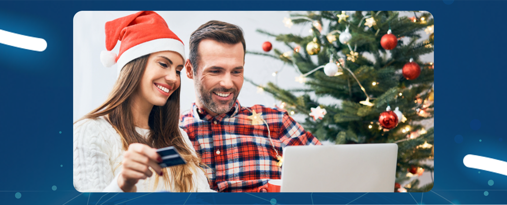 kobieta w czapce Mikołaja i mężczyzna siedzą przy choince i ogląda coś na laptopie